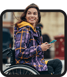 A woman in a wheelchair smiling and holding a cell phone, representing new arrival or resettlement.